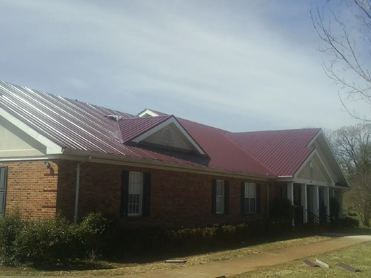 Red metal roof with gabled entries on a long brick building, from a Hail Damage Roof Repair job in Sauk Rapids