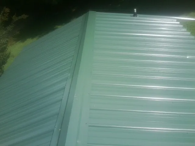 New green metal panels meeting at the ridge of a roof — Flat Roof Repair work by our crew in Sauk Rapids