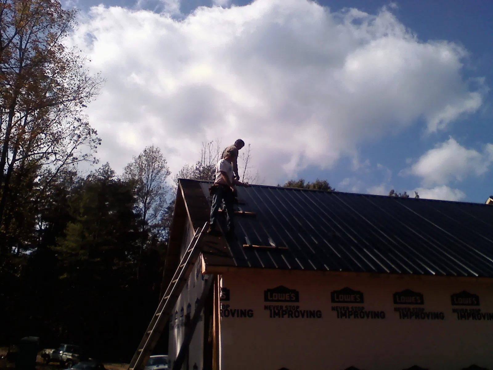 Roofer fastening dark metal panels high against a cloudy sky, from a Roof Inspection job in Sauk Rapids