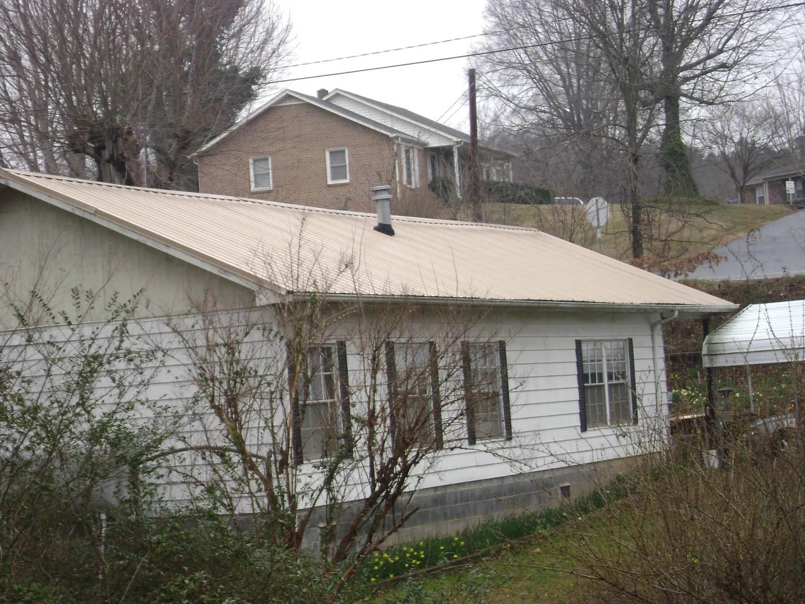 Tan metal roof on a white sided house set into a hillside — Commercial Roofing by Roofing Brothers in Sauk Rapids