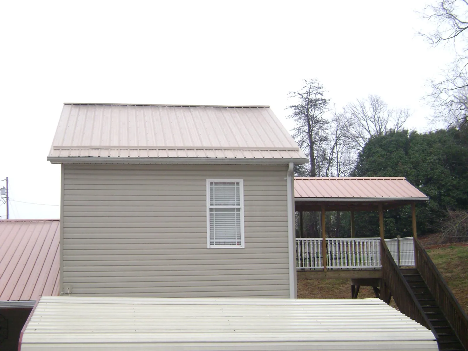 Tan metal roofs on a two story addition and attached porch, from a Roof Replacement job in Sauk Rapids
