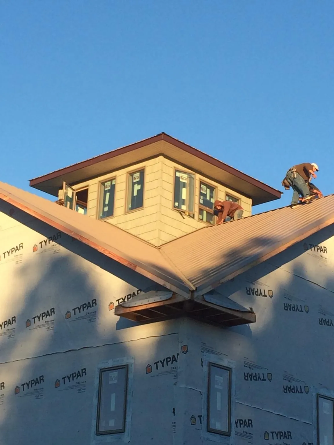 Roofers working around a rooftop cupola on a new metal roof at sunset — Roof Waterproofing in Sauk Rapids by Roofing Brothers